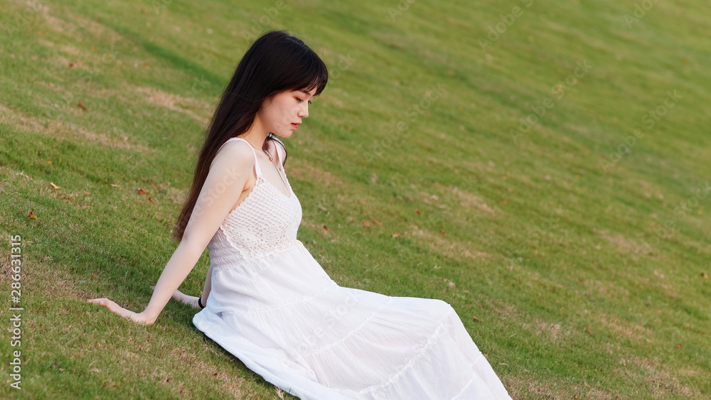 Portrait of beautiful Chinese young woman in white wedding dress sitting on grass field with hand on ground, beauty in summer. Portrait of beautiful Chinese young woman in white wedding dress sitting on grass field with hand on ground, beauty in summer.