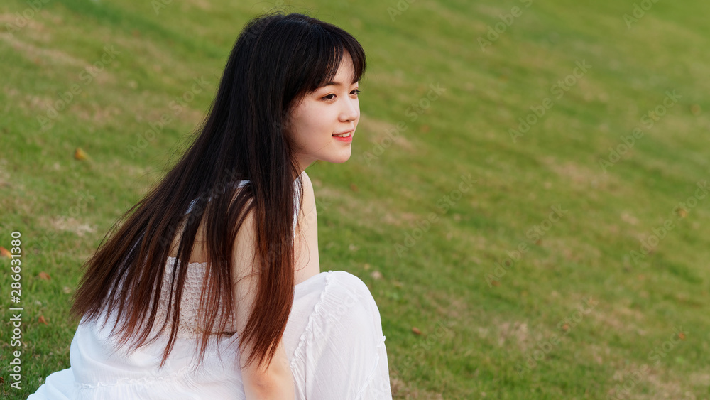 Portrait of beautiful Chinese young woman in white wedding dress sitting on grass field with hands on her leg, beauty in summer. Portrait of beautiful Chinese young woman in white wedding dress sitting on grass field with hands on her leg, beauty in summer.