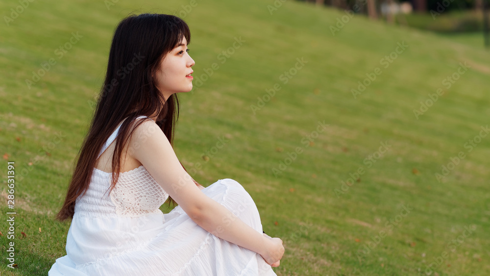 Portrait of beautiful Chinese young woman in white wedding dress sitting on grass field with hands on her leg, beauty in summer. Portrait of beautiful Chinese young woman in white wedding dress sitting on grass field with hands on her leg, beauty in summer.