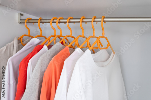 Coral and White colour clothes on hangers in wardrobe in dressing room. Several blouses and shirts for casual outfit. Fashion  background with copy space.