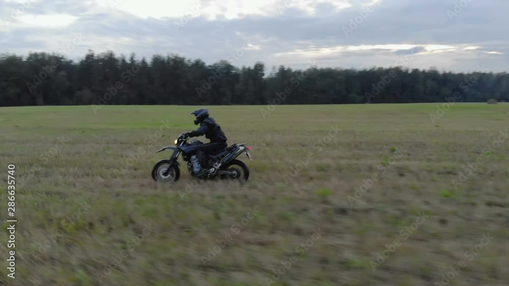 Aerial shot extreme driving Enduro over rough terrain. A man in black protective gear controls a motorcycle riding at high speed on the field along the forest