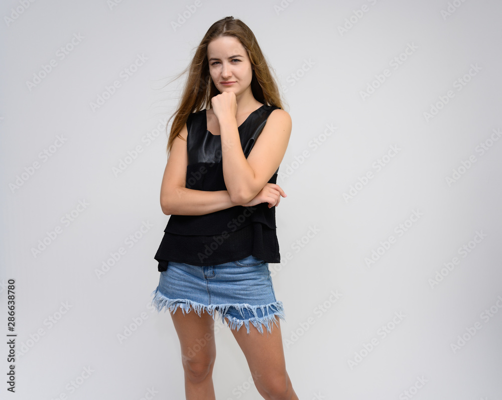 Studio photo portrait of a pretty student girl, young brunette woman with long beautiful hair in denim shorts and a black T-shirt on a white background. Smiling, talking, showing emotions Studio photo portrait of a pretty student girl, young brunette woman with long beautiful hair in denim shorts and a black T-shirt on a white background. Smiling, talking, showing emotions
