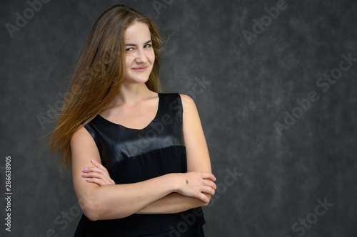 Studio photo portrait of a pretty student girl, brunette young woman with long beautiful hair in a black T-shirt on a gray background. Smiling, talking, showing emotions