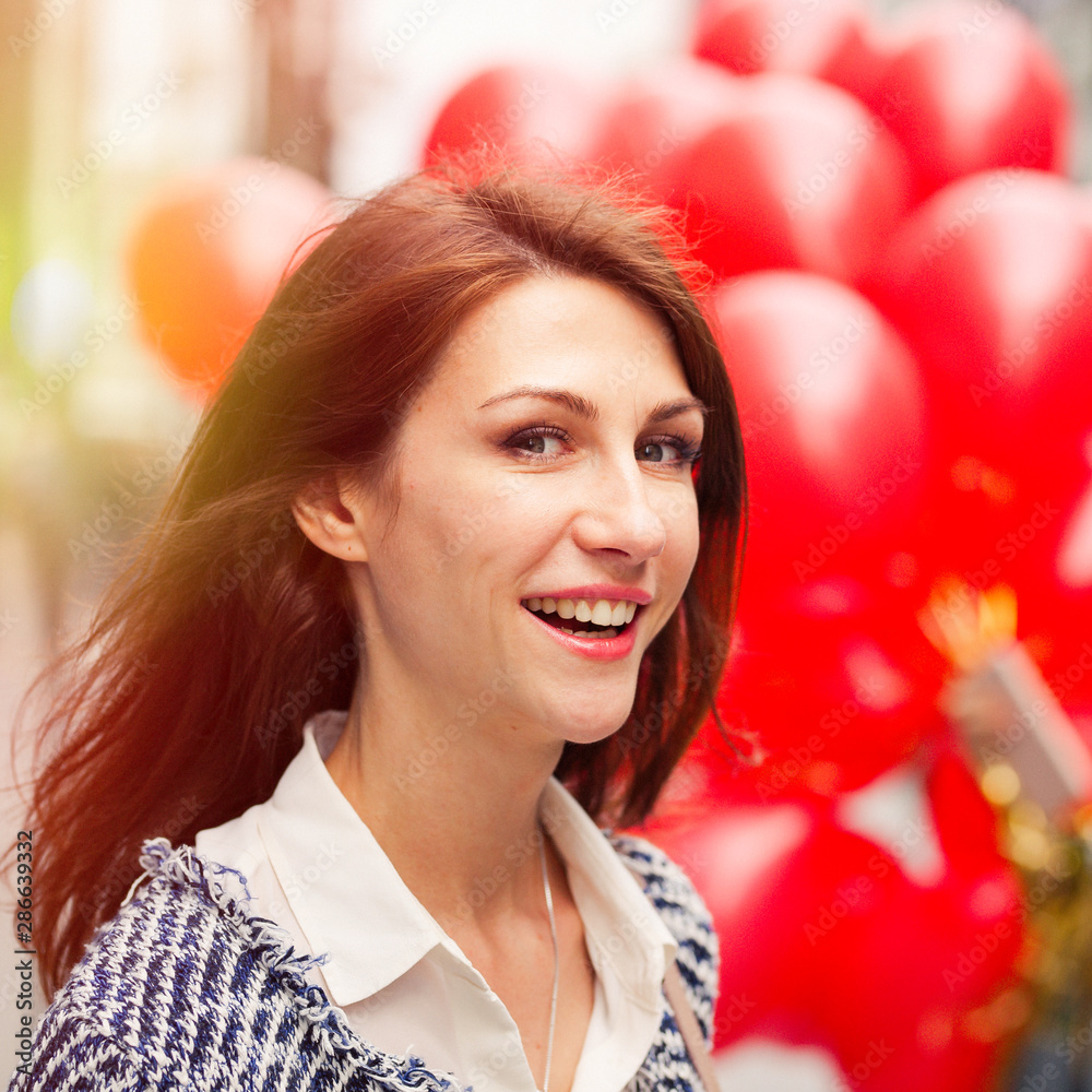 Close portrait of a smiling happy beautiful brunette young woman. a bunch of red balloons in the background. Warm sunlight. Happiness, joy, fun, holiday. Close portrait of a smiling happy beautiful brunette young woman. a bunch of red balloons in the background. Warm sunlight. Happiness, joy, fun, holiday.