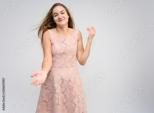 Studio portrait of a knee-length of a pretty girl student, brunette young woman with long beautiful hair in a pink dress on a white background. Smiling, talking, showing emotions photo