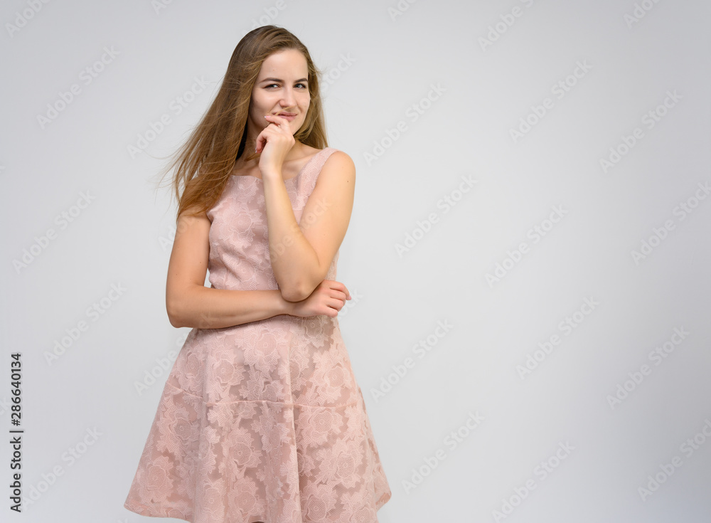 Studio portrait of a knee-length of a pretty girl student, brunette young woman with long beautiful hair in a pink dress on a white background. Smiling, talking, showing emotions