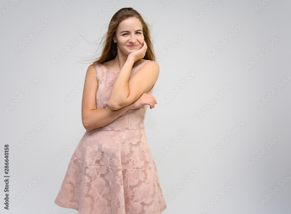 Studio portrait of a knee-length of a pretty girl student, brunette young woman with long beautiful hair in a pink dress on a white background. Smiling, talking, showing emotions Studio portrait of a knee-length of a pretty girl student, brunette young woman with long beautiful hair in a pink dress on a white background. Smiling, talking, showing emotions