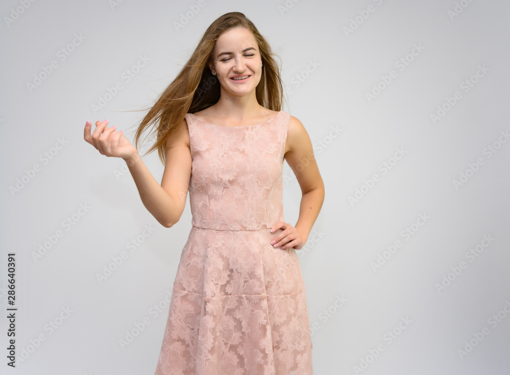 Studio portrait of a knee-length of a pretty girl student, brunette young woman with long beautiful hair in a pink dress on a white background. Smiling, talking, showing emotions