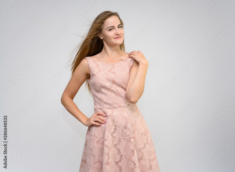 Studio portrait of a knee-length of a pretty girl student, brunette young woman with long beautiful hair in a pink dress on a white background. Smiling, talking, showing emotions Studio portrait of a knee-length of a pretty girl student, brunette young woman with long beautiful hair in a pink dress on a white background. Smiling, talking, showing emotions