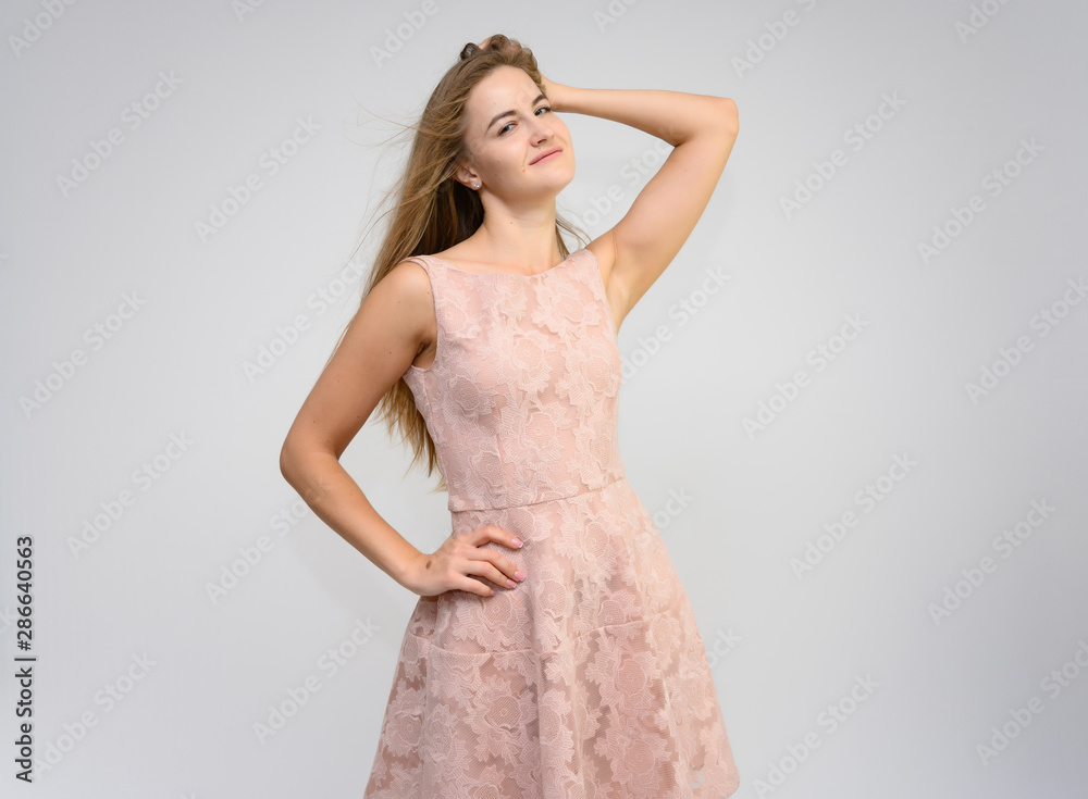 Studio portrait of a knee-length of a pretty girl student, brunette young woman with long beautiful hair in a pink dress on a white background. Smiling, talking, showing emotions Studio portrait of a knee-length of a pretty girl student, brunette young woman with long beautiful hair in a pink dress on a white background. Smiling, talking, showing emotions