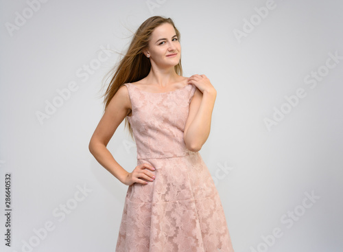 Studio portrait of a knee-length of a pretty girl student, brunette young woman with long beautiful hair in a pink dress on a white background. Smiling, talking, showing emotions