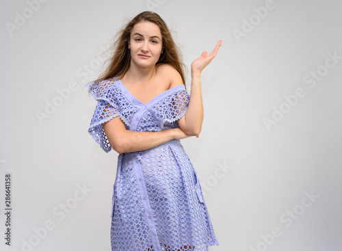 Studio portrait of a knee-length of a pretty girl student, brunette young woman with long beautiful hair in a dress on a white background. Smiling, talking, showing emotions photo
