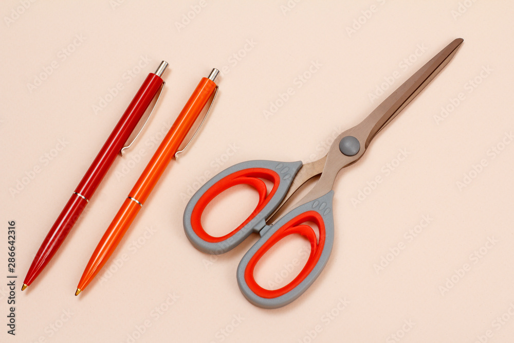 Two pens and scissors on a beige background. Two pens and scissors on a beige background.