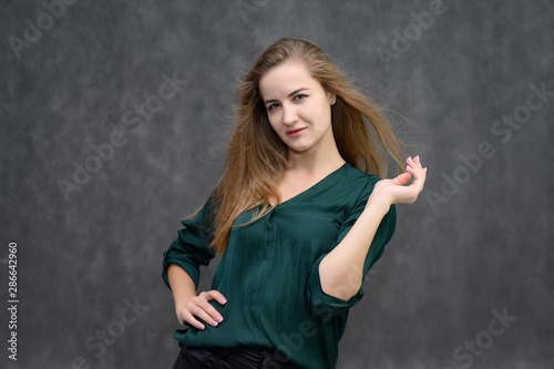 Studio portrait on the waist of a pretty student girl, a young brunette woman with long beautiful hair in a green blouse on a gray background. Smiling, talking, showing emotions