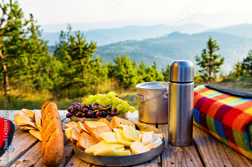 Small snack in the mountains. Cheese, grapes and baguette on top of wooden table, with mountains in the distance. photo