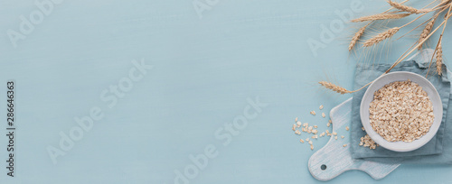 bowl of dry oat flakes with ears of wheat on light blue background. Cooking oats porridge concept. photo