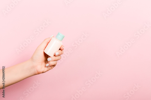 Female hand holding cream bottle of lotion isolated. Girl give tube cosmetic products on pink background