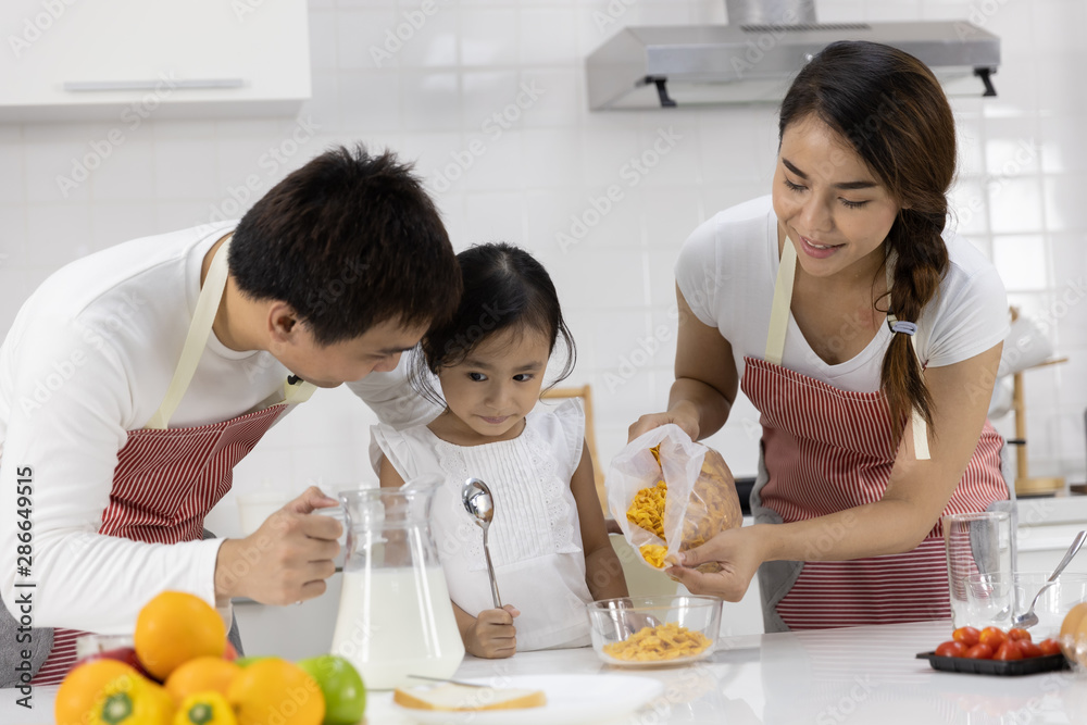 Happy Asian family make a cooking. Father and Mother make breakfast, cereal with milk give daughter in the kitchen at home. Healthy food concept For the strength of the body