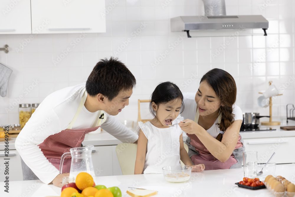 Happy Asian family make a cooking. Father, Mother and Daughter are eating breakfast, cereal with milk in the kitchen at home. Healthy food concept and happy holidays