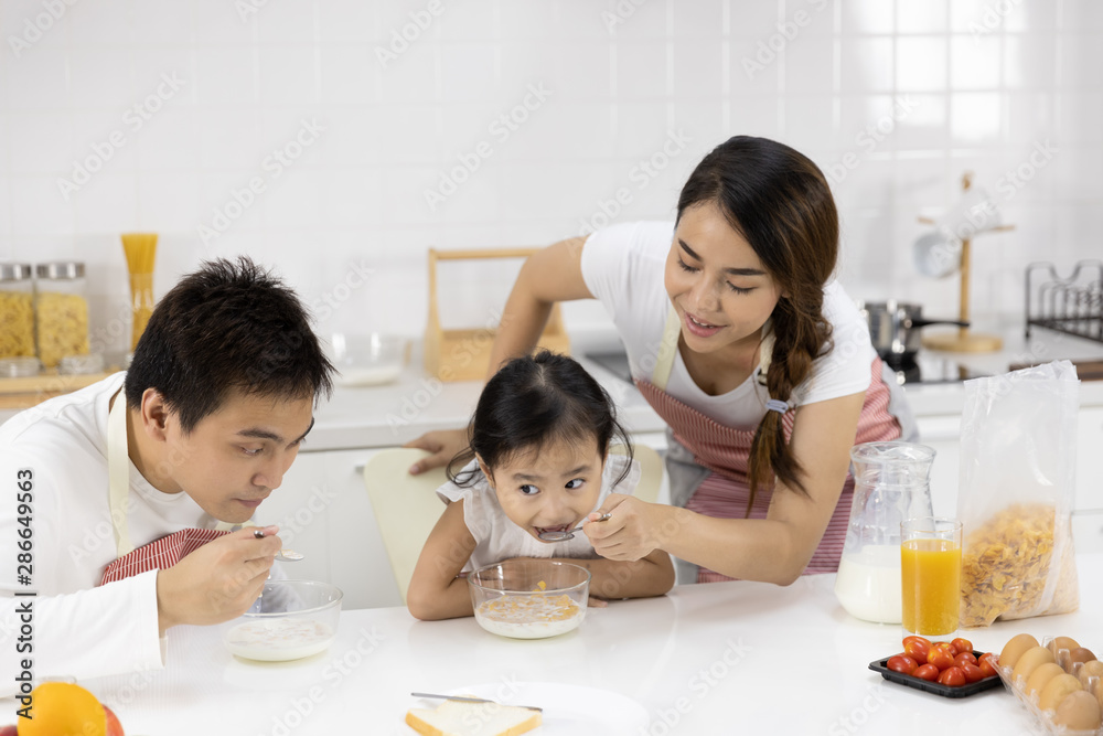 Happy Asian family make a cooking. Father, Mother and Daughter are eating breakfast, cereal with milk in the kitchen at home. Healthy food concept and happy holidays Happy Asian family make a cooking. Father, Mother and Daughter are eating breakfast, cereal with milk in the kitchen at home. Healthy food concept and happy holidays
