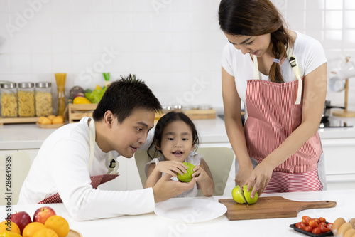 Happy Asian family make a cooking. Father, Mother and Daughter are preparing fruit, green apple in the kitchen at home. Healthy food concept and happy holidays