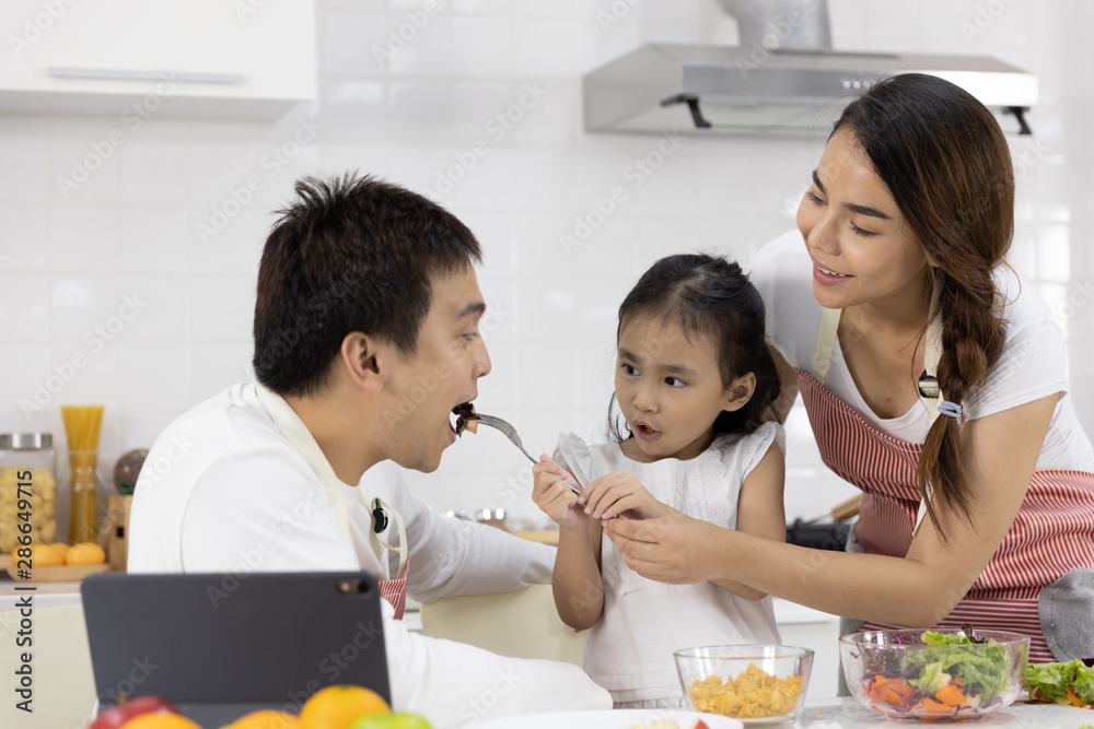 Happy Asian family make a cooking. Father, Mother and Daughter are eating salad, vegetable in the kitchen at home. Healthy food concept and happy holidays Happy Asian family make a cooking. Father, Mother and Daughter are eating salad, vegetable in the kitchen at home. Healthy food concept and happy holidays