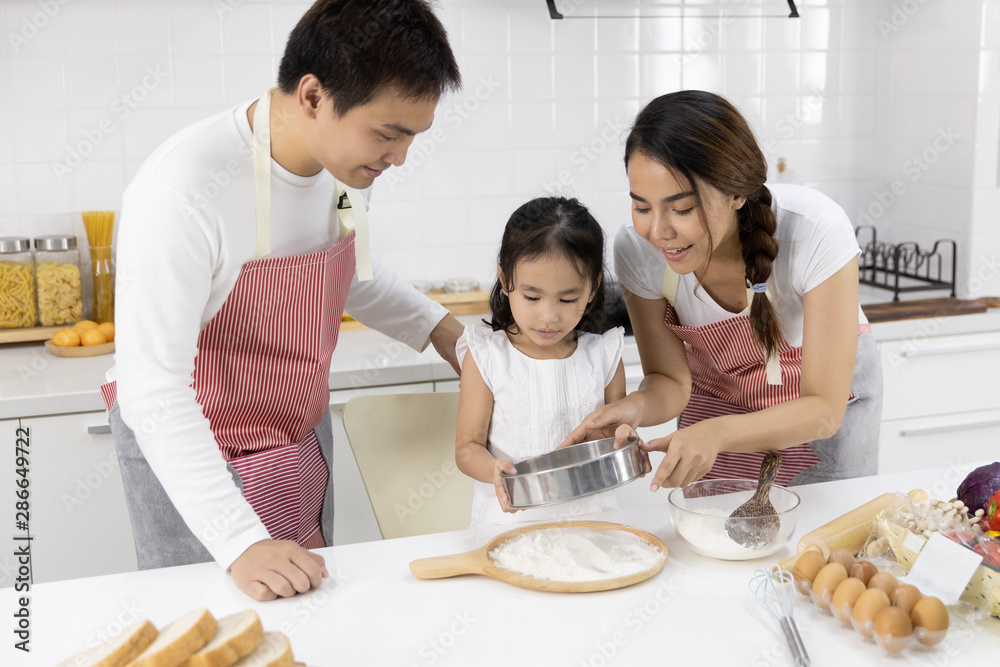Happy Asian family Father, Mother and Daughter are sieving flour preparing the dough, bake cookies in the kitchen. family cooking food Concept. Happy Asian family Father, Mother and Daughter are sieving flour preparing the dough, bake cookies in the kitchen. family cooking food Concept.