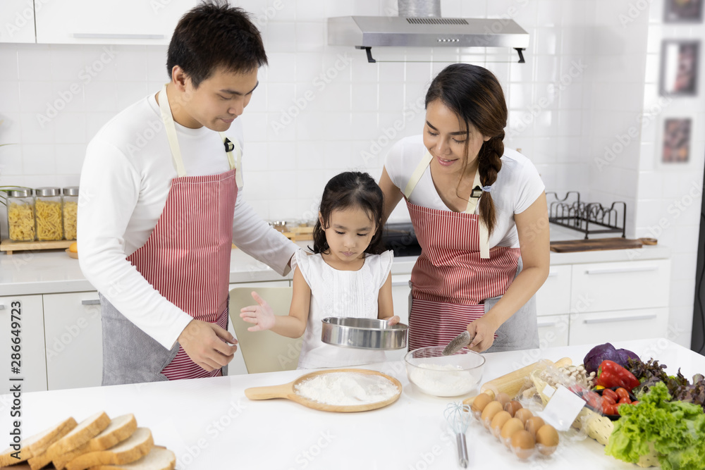 Happy Asian family Father, Mother and Daughter are sieving flour preparing the dough, bake cookies in the kitchen. family cooking food Concept. Happy Asian family Father, Mother and Daughter are sieving flour preparing the dough, bake cookies in the kitchen. family cooking food Concept.