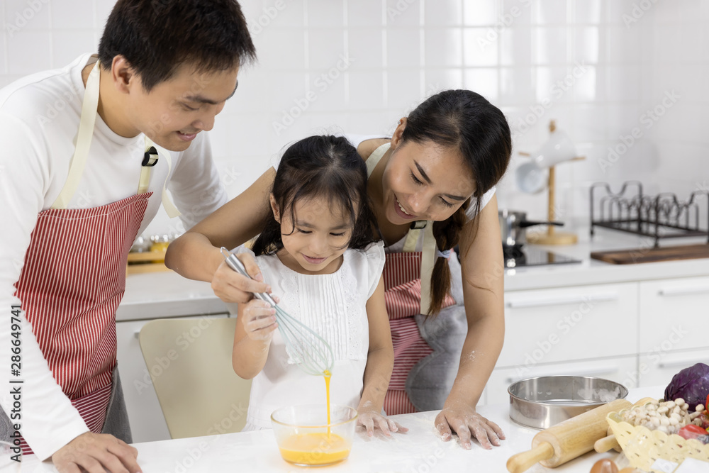 Happy Asian family Father, Mother and Daughter are beat eggs in bowl preparing the cookies in the kitchen. family cooking food Concept. Happy Asian family Father, Mother and Daughter are beat eggs in bowl preparing the cookies in the kitchen. family cooking food Concept.