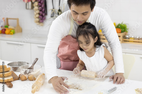 Happy Asian family Father and Daughter are rolling pin thresh flour for making bakery in the kitchen in home. family cooking food Concept.