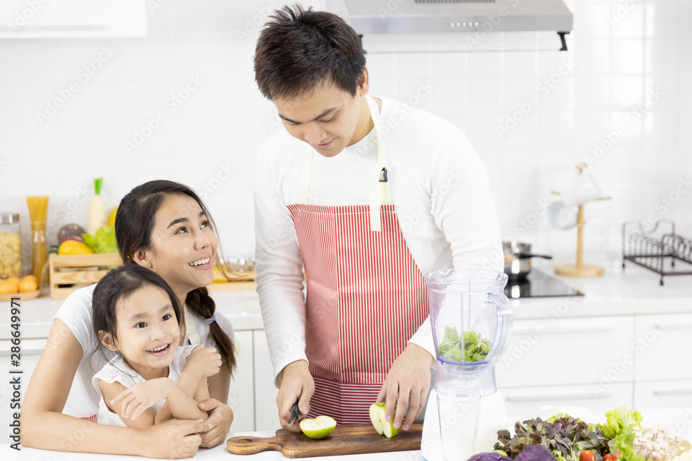 Happy Asian family in the kitchen. Father, Mother and Daughter are preparing the salad in blender Menu tasty smoothie and ingredients on table at home. Cooking food, Healthy food concept Happy Asian family in the kitchen. Father, Mother and Daughter are preparing the salad in blender Menu tasty smoothie and ingredients on table at home. Cooking food, Healthy food concept