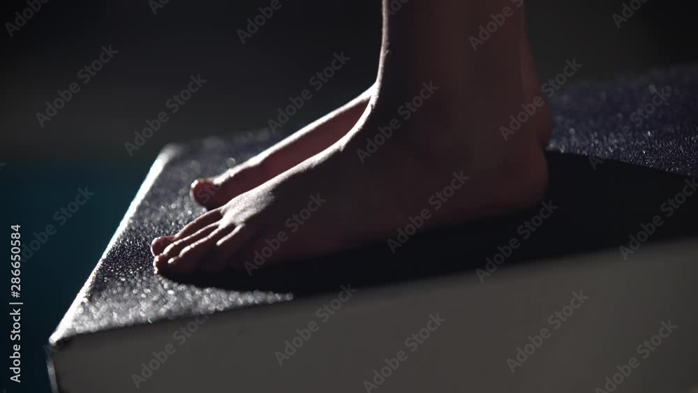 Close up shot of a professional female swimmer's feet preparing to jump off the starting block into the swimming pool. Night shot