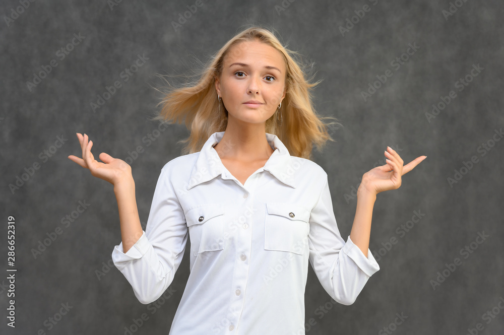 Studio portrait of a pretty blonde student girl, young woman in a white shirt on a gray background. Talking, showing emotions. Studio portrait of a pretty blonde student girl, young woman in a white shirt on a gray background. Talking, showing emotions.