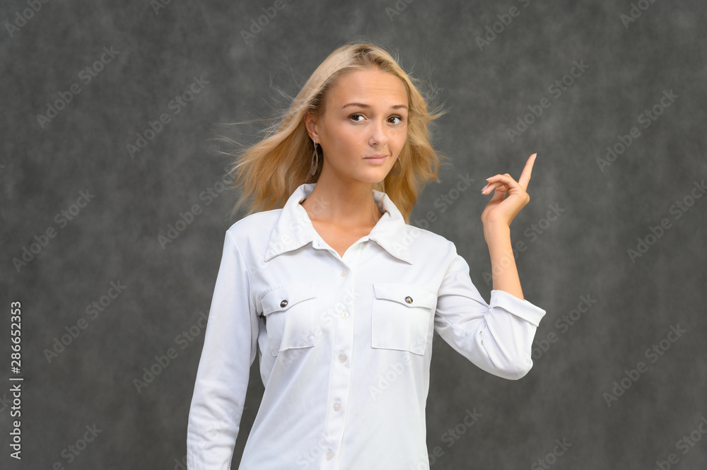 Studio portrait of a pretty blonde student girl, young woman in a white shirt on a gray background. Talking, showing emotions. Studio portrait of a pretty blonde student girl, young woman in a white shirt on a gray background. Talking, showing emotions.