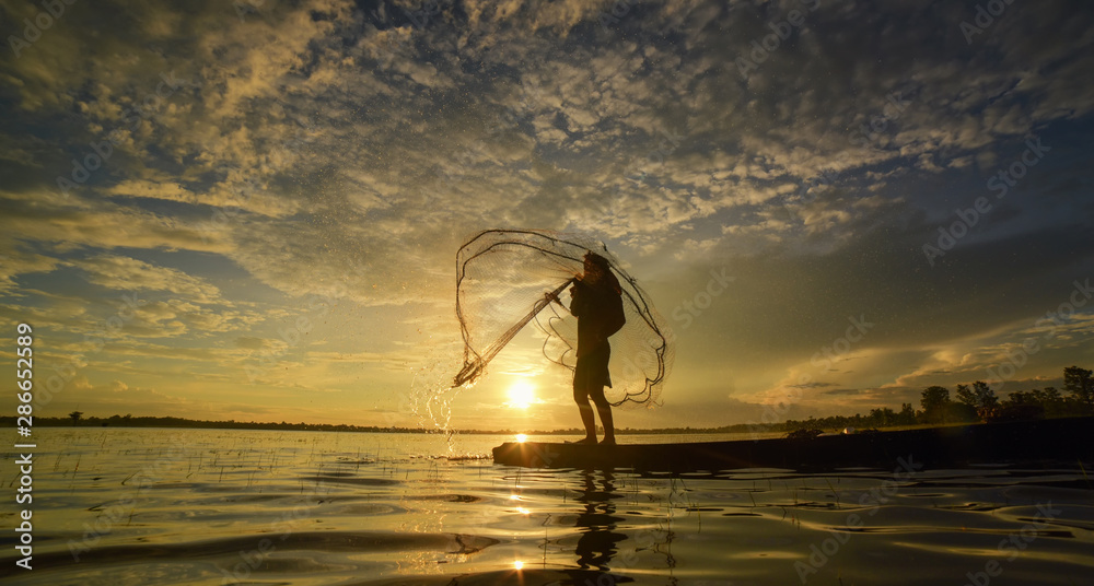 Silhouette of fisherman throwing fishing net during sunrise. Silhouette of  man catching the fish in twilight, Thailand. Stock Photo