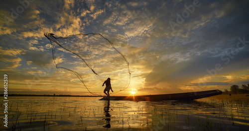 Silhouette of fisherman throwing fishing net during sunrise. Silhouette of man catching the fish in twilight, Thailand.