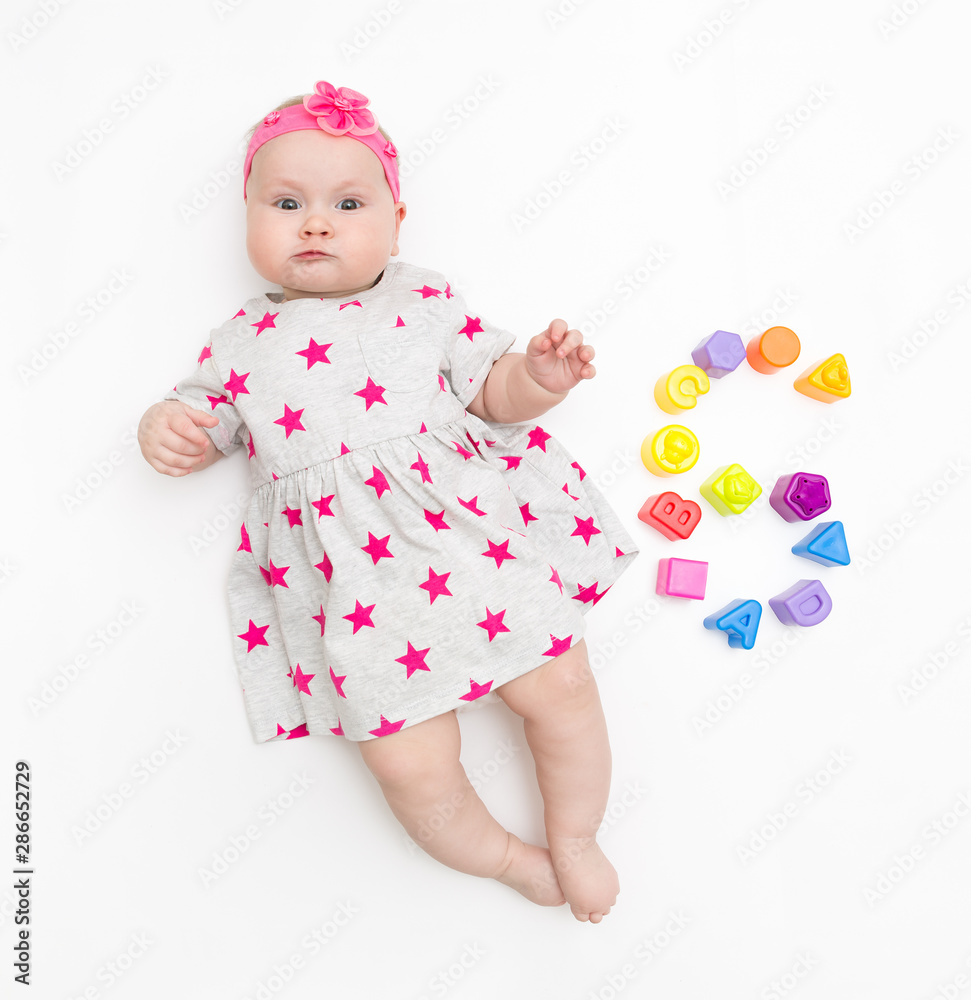 Portrait of a sweet infant baby girl wearing a pink dress and headband bow, isolated on white in studio with number six from toys Portrait of a sweet infant baby girl wearing a pink dress and headband bow, isolated on white in studio with number six from toys