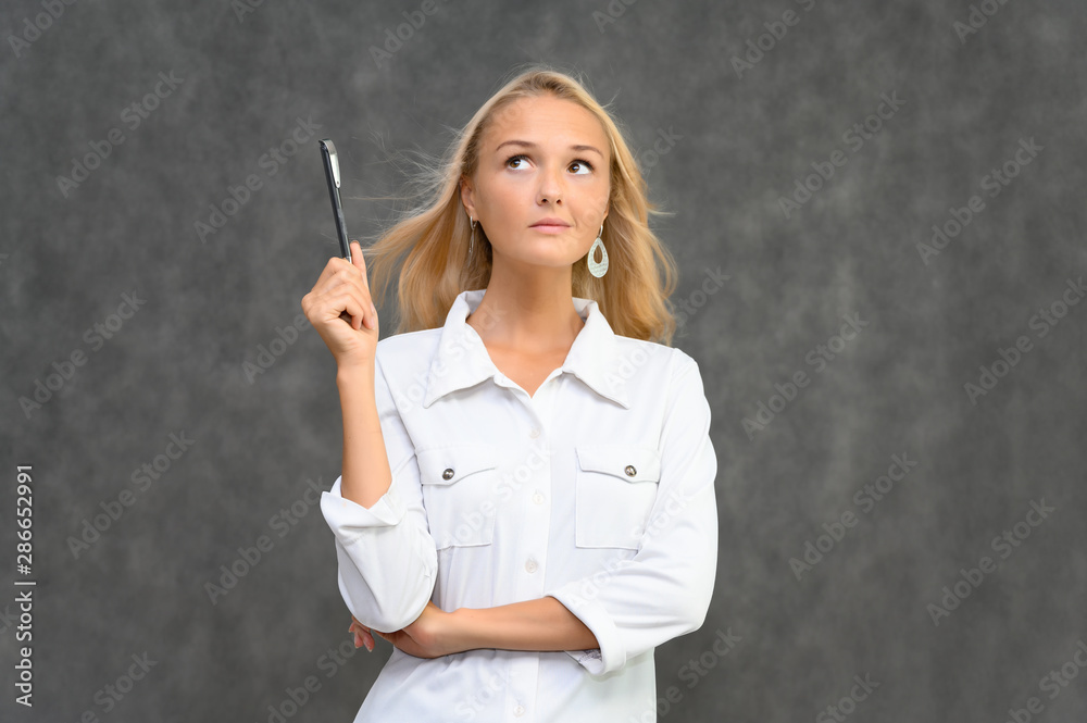 Studio portrait of a pretty blonde student girl, young woman in a white shirt on a gray background. Talking, showing emotions. Studio portrait of a pretty blonde student girl, young woman in a white shirt on a gray background. Talking, showing emotions.
