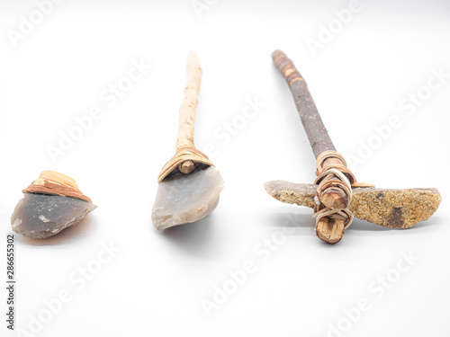 Replicas of the primal stone tools with wooden handles and leather strapping isolated on white background. Primitive stone axe, dagger and hammer: weapons of the prehistoric peoples.Selected focus. © Konstantin Belov