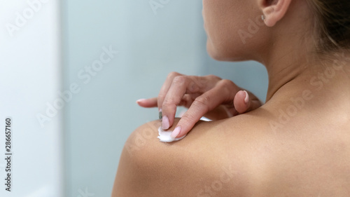 Woman applying body cream on shoulder in bathroom © brizmaker
