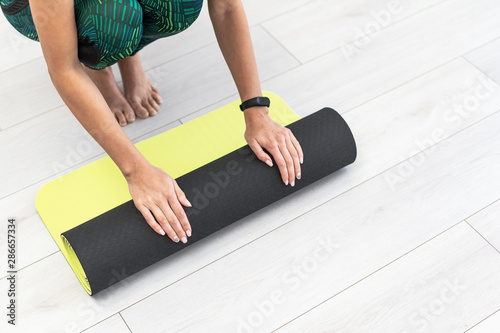 Young sporty woman rolling fitness mat on the floor