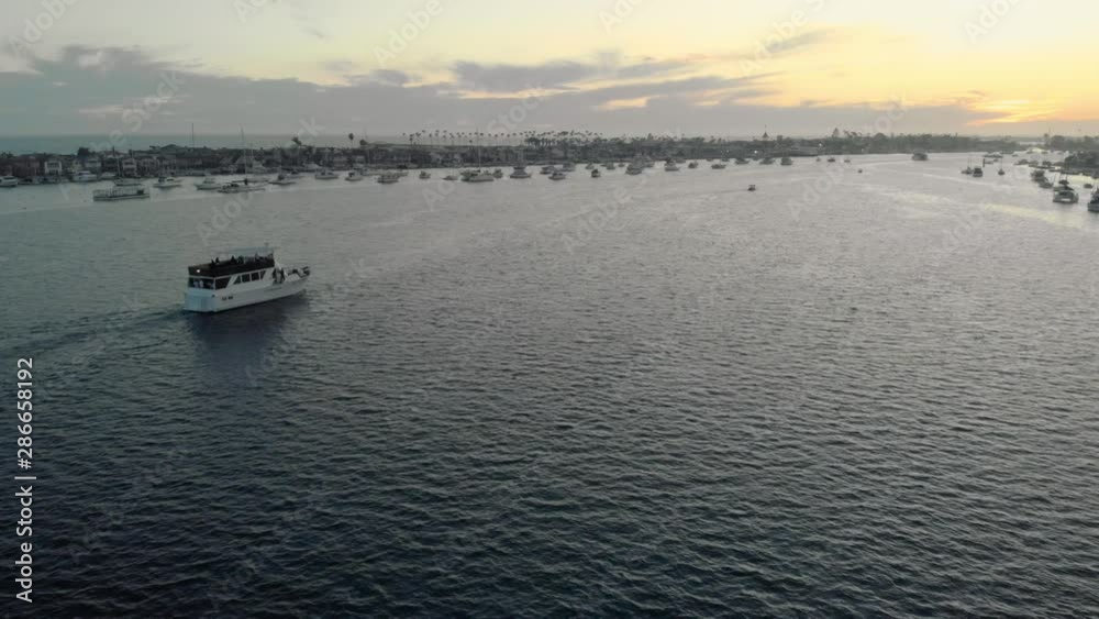 Yacht sailing in marina at sunset golden hour. Drone follow shot from a distance. Newport Bay in Newport Beach, Orange County, California. Closing scene. Yacht sailing in marina at sunset golden hour. Drone follow shot from a distance. Newport Bay in Newport Beach, Orange County, California. Closing scene.