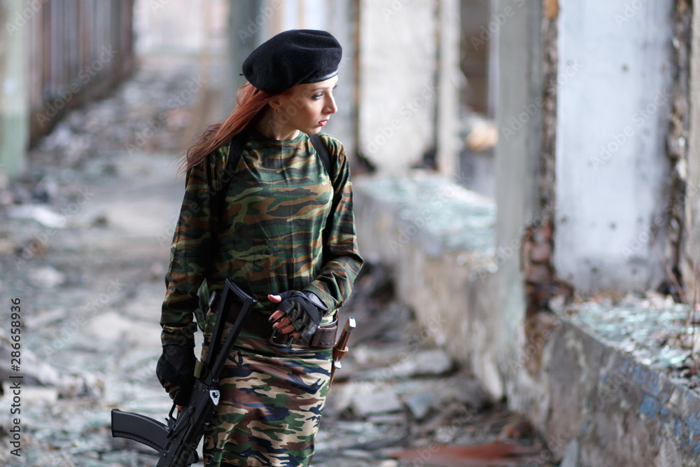 Fototapeta premium Soldier girl with weapons in camouflage uniform in a destroyed building. The concept of service in the army, the girl in the army and in the war.