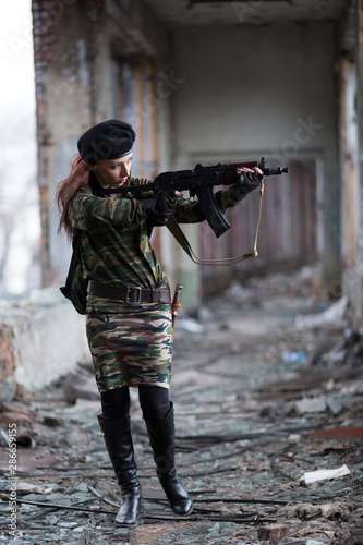 Soldier girl with weapons in camouflage uniform in a destroyed building. The concept of service in the army, the girl in the army and in the war.