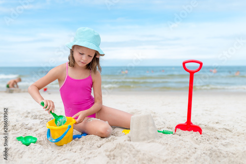Happy child girl playing with sand at the beach in summer