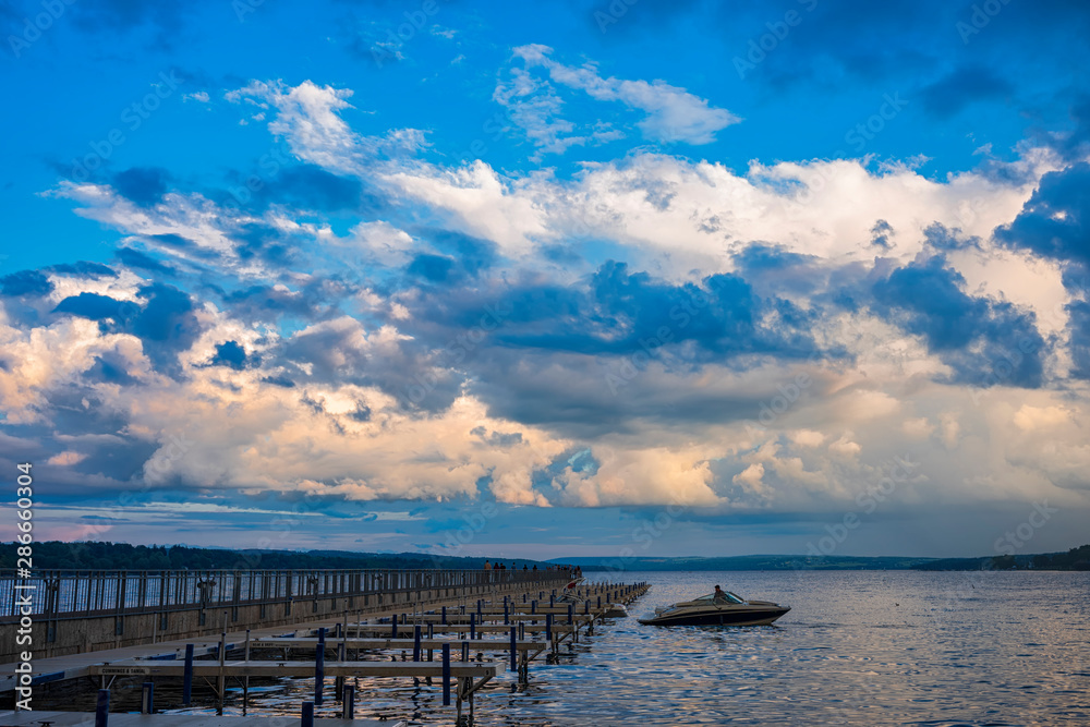A motorboat docks at the public boat dock and pier in Skaneateles Lake, Skaneateles, in the Fingerlakes Region of New York State around the time of a summer sunset in August . A motorboat docks at the public boat dock and pier in Skaneateles Lake, Skaneateles, in the Fingerlakes Region of New York State around the time of a summer sunset in August .
