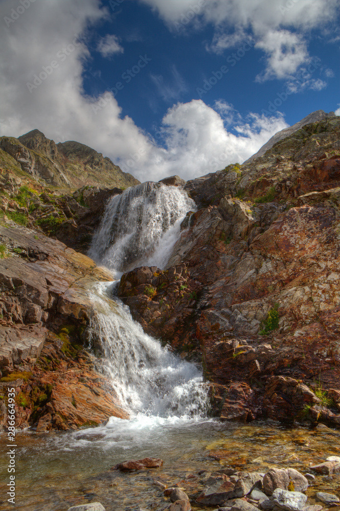 Obraz premium Small waterfall over red colored rocks and boulders, splashing in a small lake