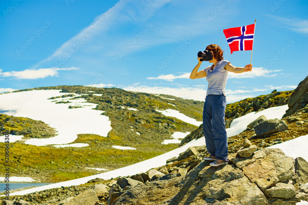 Obraz premium Tourist holds camera and norwegian flag in mountains