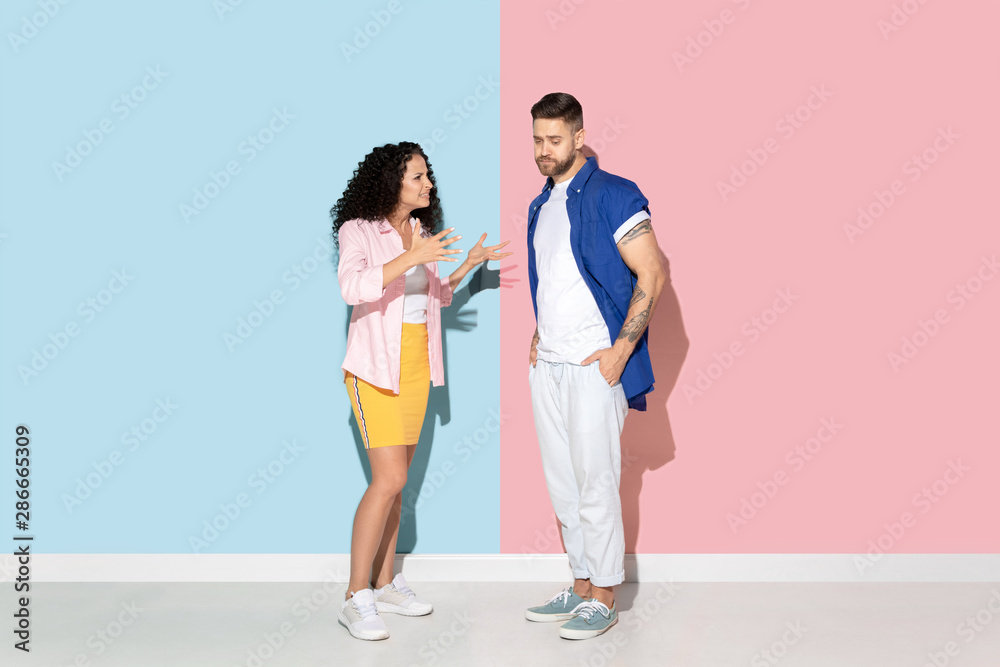 Young emotional caucasian couple in bright casual clothes posing on pink and blue background. Concept of human emotions, facial expession, relations, ad. Woman angry talking to man, he's sad. Young emotional caucasian couple in bright casual clothes posing on pink and blue background. Concept of human emotions, facial expession, relations, ad. Woman angry talking to man, he's sad.