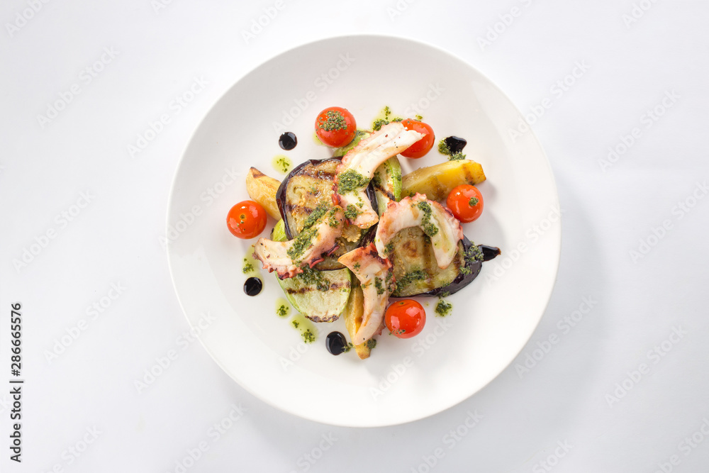 grilled octopus with zucchini, tomato and eggplant on white plate isolated on white background